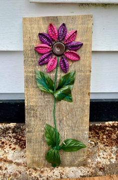 a purple flower is painted on a wooden board with green leaves and brown button in the center