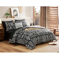 a bed with black and white bedspread on top of a wooden floor next to a window