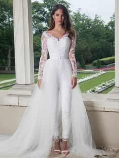 a woman standing in front of columns wearing a white wedding gown with long sleeves and sheer tulle