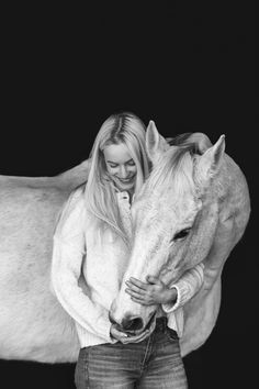 a black and white photo of a woman hugging a horse in front of a dark background