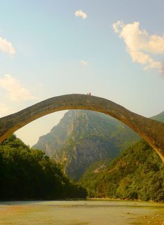 an old stone bridge over a river with mountains in the background