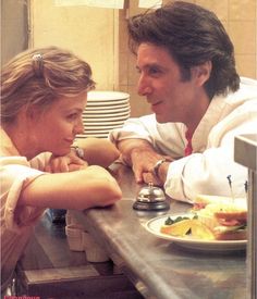 a man and woman sitting at a counter in a restaurant kitchen talking to each other