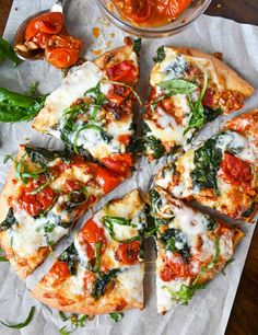 a pizza with spinach, tomatoes and cheese cut into slices on a piece of parchment paper