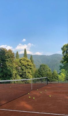 a tennis court with several balls on it and trees in the background, surrounded by mountains