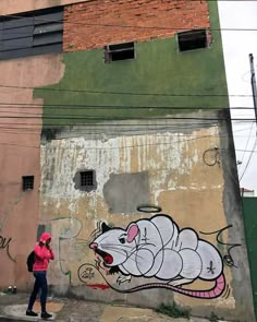 a woman walking down the street in front of a building with graffiti on it's side