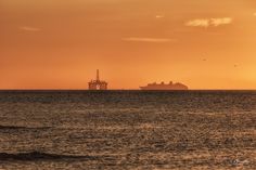 the sun is setting over an ocean with a ship in the distance