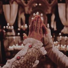 two people holding their hands together in front of some lit candles and chandeliers