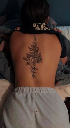 a woman laying in bed with her back turned to the camera and tattoos on her lower back