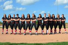 a group of women in black and red uniforms posing for a photo on a baseball field