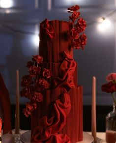 a three tiered red wedding cake with flowers on the top and candles in the background