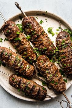 several skewers of meat on a plate with green garnishes and tongs