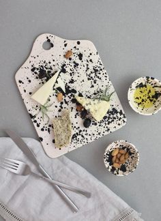 an assortment of cheeses and crackers on a white plate next to silverware