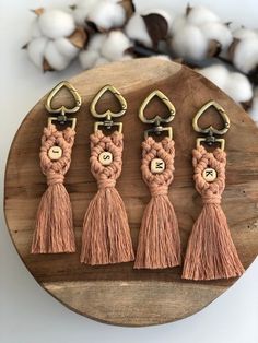 four tasseled key chains with gold hardware and metal hooks on a wooden board