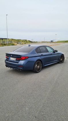 a blue car parked on the side of an empty parking lot next to some grass