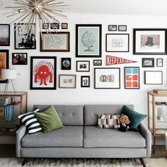 a living room filled with lots of framed pictures on the wall above a gray couch