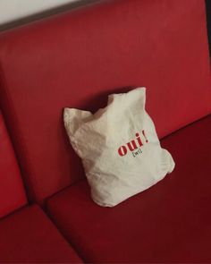 a white bag sitting on top of a red couch with the word oui printed on it