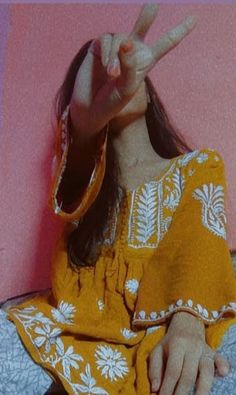 a doll sitting on top of a bed making the peace sign with her hand and wearing a yellow dress