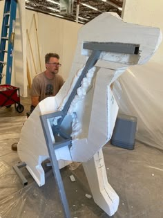 a man standing next to a large white object in a room filled with construction materials