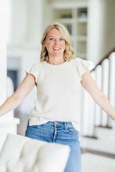 a woman standing in front of a white couch holding her arms out to the side