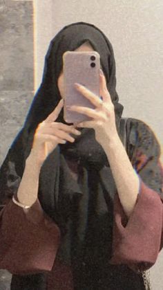 a woman taking a selfie in front of a mirror wearing a hijab