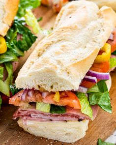 a sub sandwich with lettuce, tomato, corn and other toppings on a cutting board