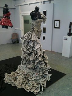 a dress made out of newspapers sitting on top of a black piece of paper in a room