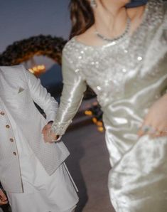 a man and woman dressed in white holding hands