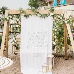 a white wedding sign with greenery and flowers on it next to a wooden swing