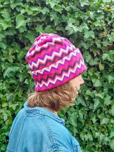 a woman wearing a pink and purple hat standing in front of green leaves on a sunny day