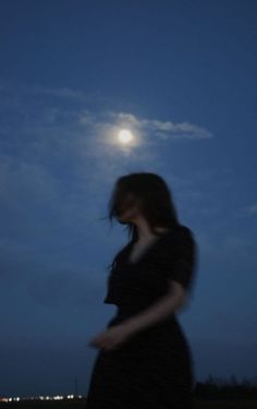 a woman standing in front of the moon with her hand on her hip and looking down