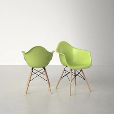 two green chairs sitting next to each other on top of a cement floor in front of a white wall