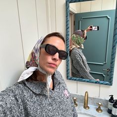 a woman taking a selfie in front of a bathroom mirror with her scarf wrapped around her head