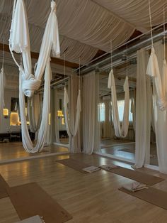 an empty room with white drapes hanging from the ceiling and yoga mats on the floor