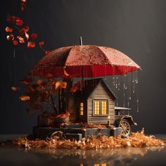 a small house under an umbrella with autumn leaves surrounding it and falling on the ground