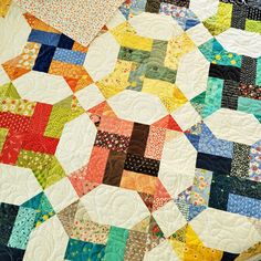 a quilted table topper with many different colors and patterns on it, sitting on a wooden surface