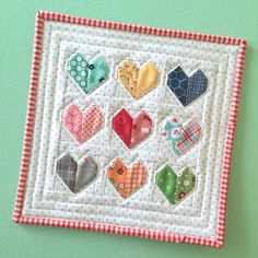 a close up of a quilted wall hanging on a green wall with hearts in the center