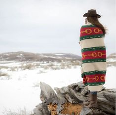 a woman standing on top of a log in the snow wearing a sweater and hat