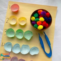 some paper cups and scissors on a table with pom - poms in them