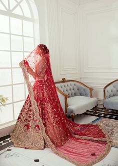 a woman in a red and gold bridal gown is looking out the window with her veil draped over her head