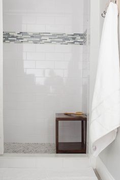 a white tiled bathroom with a wooden table and towel rack on the wall next to it