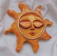 a ceramic sun with eyes closed on a white cloth background is featured in this image