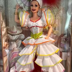 a barbie doll in a glass case wearing a white dress with yellow and red trim