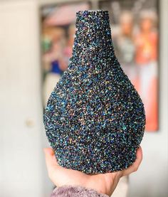 a hand holding a blue vase filled with colorful sprinkles