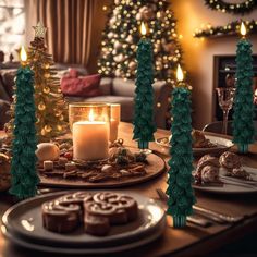 a table topped with christmas trees and cookies next to a lit candle on top of a plate