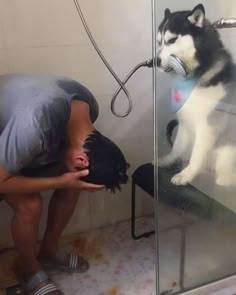 a man kneeling down next to a dog in a shower