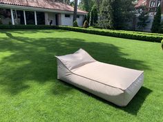 an outdoor lounge chair sitting on top of a lush green field in front of a house