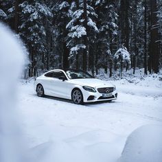 a white car parked in the middle of a snow covered road with trees behind it