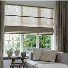 a white couch sitting under a window next to a table with two vases on it