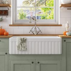 a white kitchen sink sitting under a window next to green cupboards and wooden counter tops