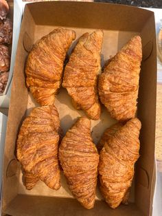 six croissants in a cardboard box with nuts on the table behind them